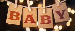 The word BABY spelled out on clothespin clipped cards in front of glowing lights.